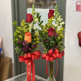 Two rose arrangements in clear glass vases with red ribbons