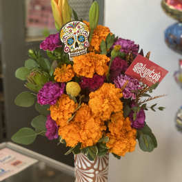 Bright orange and purple flower arrangement in a patterned vase with a skull decoration.