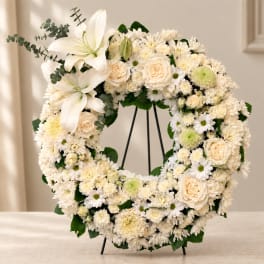 White floral wreath with lilies, roses, and daisies on a stand