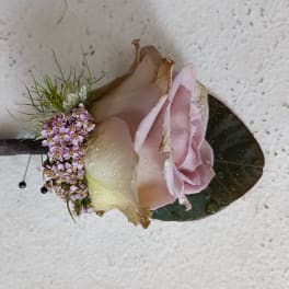 Pink rose boutonniere with small purple filler flowers and a dark leaf