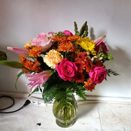 Mixed bouquet of pink roses, lilies, and orange chrysanthemums in a glass vase