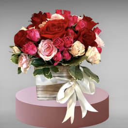 Bouquet of red, pink, and cream roses in a wooden box with a ribbon