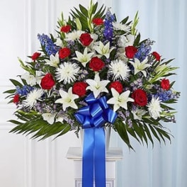 Standing floral spray with red roses, white lilies, and blue accents on a pedestal