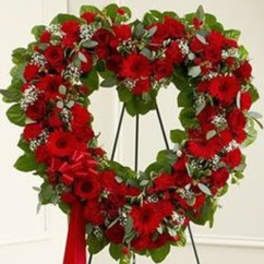 Heart-shaped red floral wreath on a stand with a red ribbon