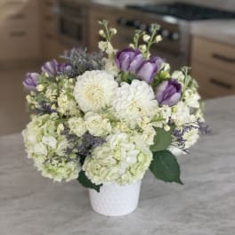 White and purple floral arrangement in a white vase