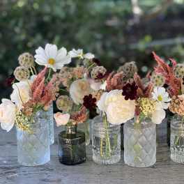 Small mixed flower arrangements in assorted glass bottles on a table