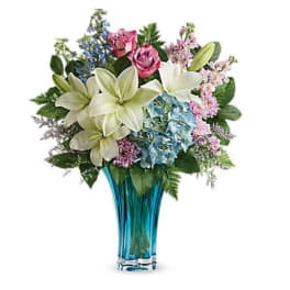 Bouquet of lilies, roses, hydrangeas, and mixed blooms in a blue glass vase