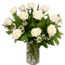 White roses arranged in a clear glass vase with fern foliage