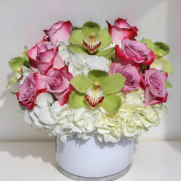 Pink roses and green orchids arranged with white hydrangeas in a white vase