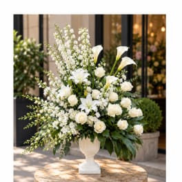 White floral arrangement in a white urn vase with roses, lilies, and calla lilies