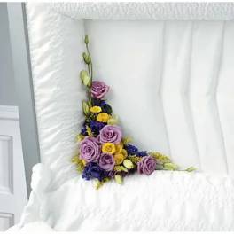 Purple roses and yellow flowers arranged in a white quilted casket interior.