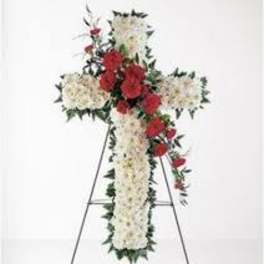 Cross-shaped floral funeral spray with white flowers and red roses on a stand