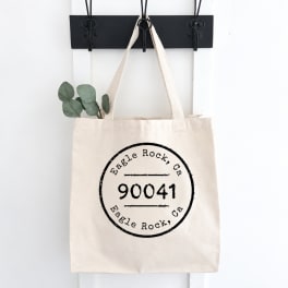 Canvas tote bag with a black printed logo hanging on a wall hook