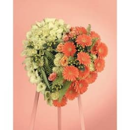 Heart-shaped floral arrangement with orange and pale green flowers on a stand