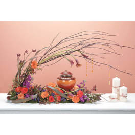 Low floral arrangement with orange and purple blooms beside white candles