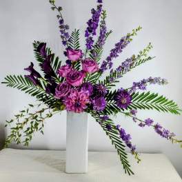 Purple roses and mixed blooms arranged in a tall white vase