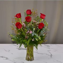 Red roses arranged in a clear glass vase with mixed greenery