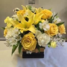 Yellow roses and lilies arranged in a black box with white accents
