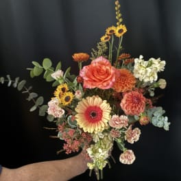 Handheld bouquet with orange and yellow flowers against a dark background.