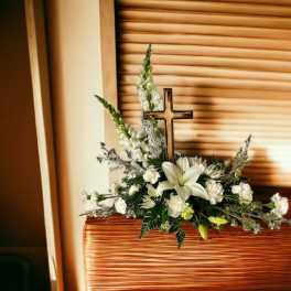 White floral arrangement with a cross in a wicker basket