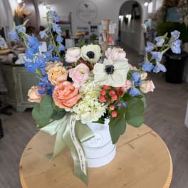 Mixed pastel bouquet in a white hatbox with blue delphinium and roses