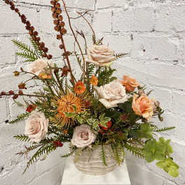 Mixed floral arrangement in a white vase with pale roses and orange blooms
