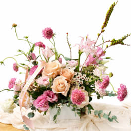 Pink and peach floral arrangement in a white box with a ribbon