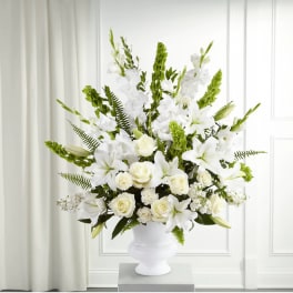 White floral arrangement in a white urn vase with green accents