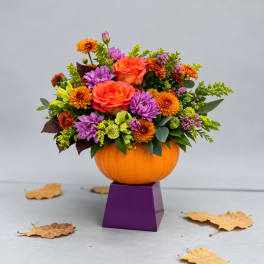 Orange and purple floral arrangement in a pumpkin-shaped container