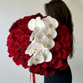 Large heart-shaped bouquet of red roses with white orchids held by a person in black clothing