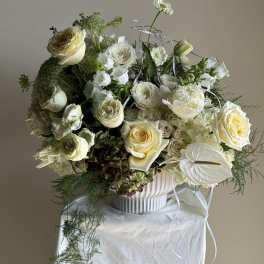 Cream and white floral arrangement in a ribbed white vase with ribbon accents