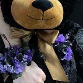 Black teddy bear with purple floral accents and a gold ribbon bow