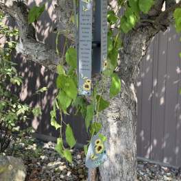 Hanging metal wind chime with butterfly and sunflower designs on a tree