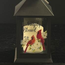 Black lantern with a candle labeled Simply Blessed and cardinals