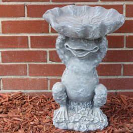 Gray garden frog statue against a brick wall