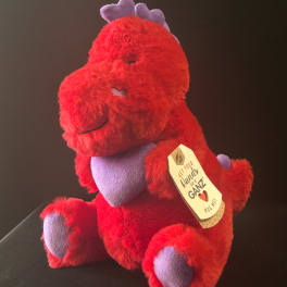 Red plush dinosaur toy with purple accents and a hanging gift tag