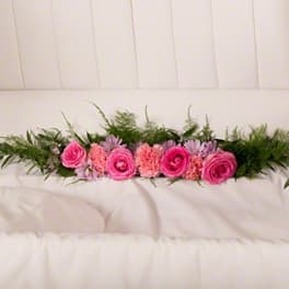 Pink roses and carnations arranged with greenery on a white couch