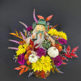 Fall floral basket with a scarecrow figure, pumpkins, and bright mums