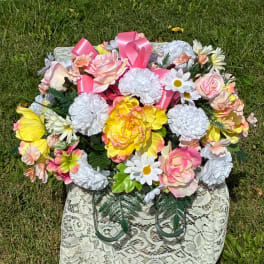 Pink and yellow floral arrangement in a lace-covered basket outdoors
