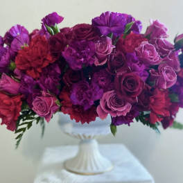 Purple and pink floral arrangement in a white pedestal vase