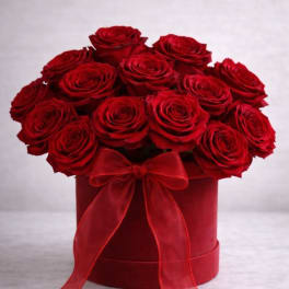 Red roses arranged in a round hatbox with a red ribbon bow