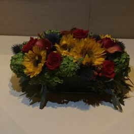 Low floral centerpiece with sunflowers, red roses, and calla lilies