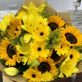 Bouquet of yellow sunflowers and lilies wrapped in newspaper-style paper