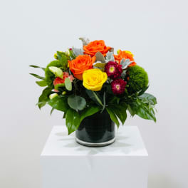 Orange and yellow roses in a glass vase with green accents