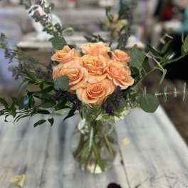 Peach rose arrangement with purple filler in a clear glass vase on a rustic wooden table