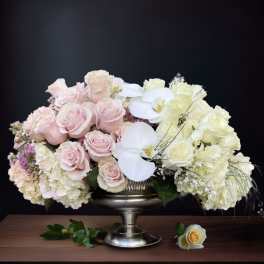 Pink and white roses with orchids in a silver pedestal vase