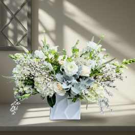 White floral arrangement in a white square vase with silver foliage