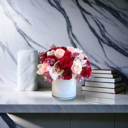 Red and blush roses arranged in a white vase beside stacked books