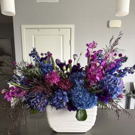 Large blue and purple floral arrangement in a white vase