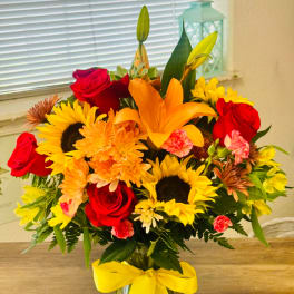 Bouquet of red roses, sunflowers, and orange lilies in a vase with a yellow ribbon